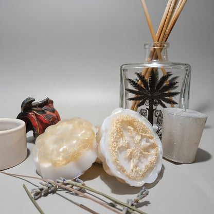 Two soap bars with a decorative bottle and candle on a textured surface