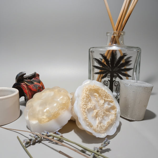 Two soap bars with a decorative bottle and candle on a textured surface
